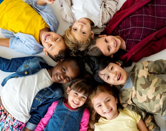 ground of children laying in circle with heads together smiling up at camera