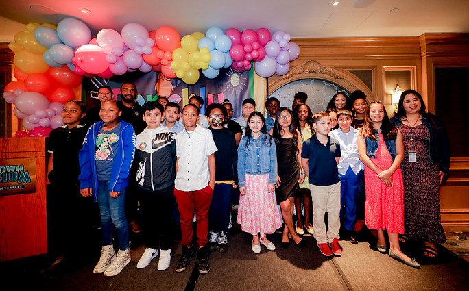 diverse group of children smiling with pink and blue baloons hung above